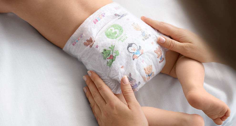 A baby is being dressed in a diaper with various animal illustrations and a size indicator.