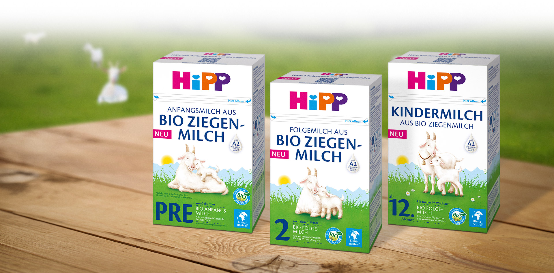 Three Hipp baby milk boxes are displayed on a wooden surface, with labels indicating different stages of baby development and the use of organic goat milk.