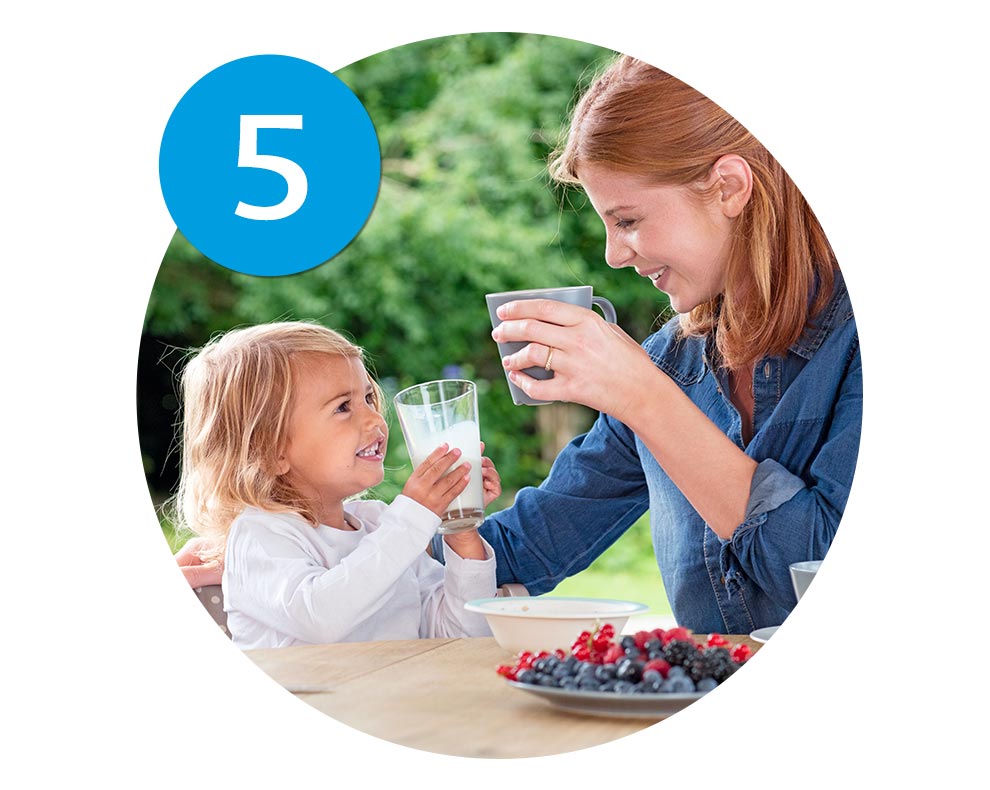 A woman and a young girl share a moment over a glass of milk and a plate of berries outdoors.