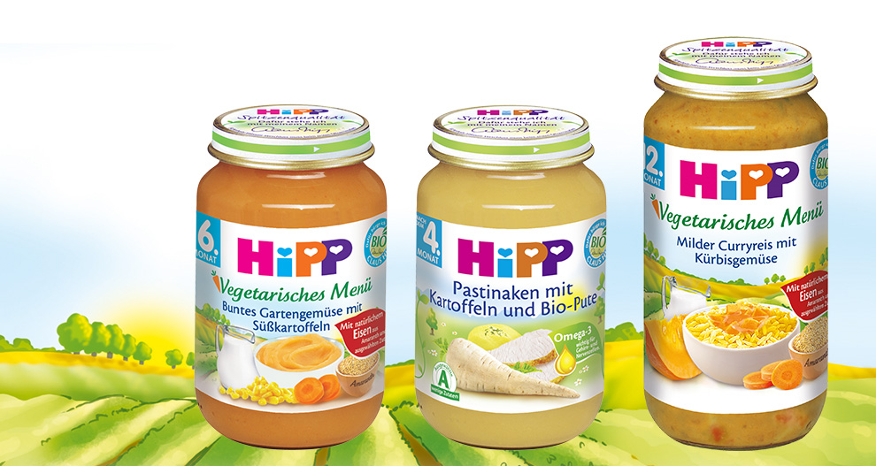 Trys stikliniai indeliai su etiketėmis, kurių kiekviename yra skirtingas maisto produktas, rodomi žalio peizažo fone.