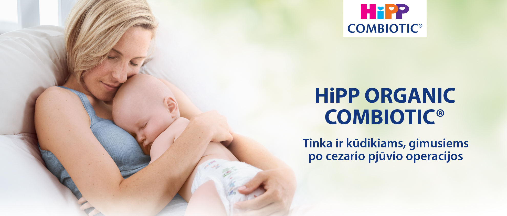 Moteris meiliai laiko kūdikį, o po juo yra užrašas "HiPP ORGANIC COMBIOTIC®" ir frazė užsienio kalba.